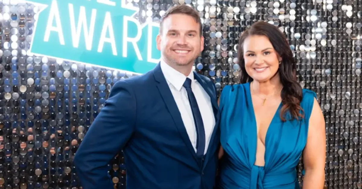 Two people smiling at an awards event, dressed formally.
