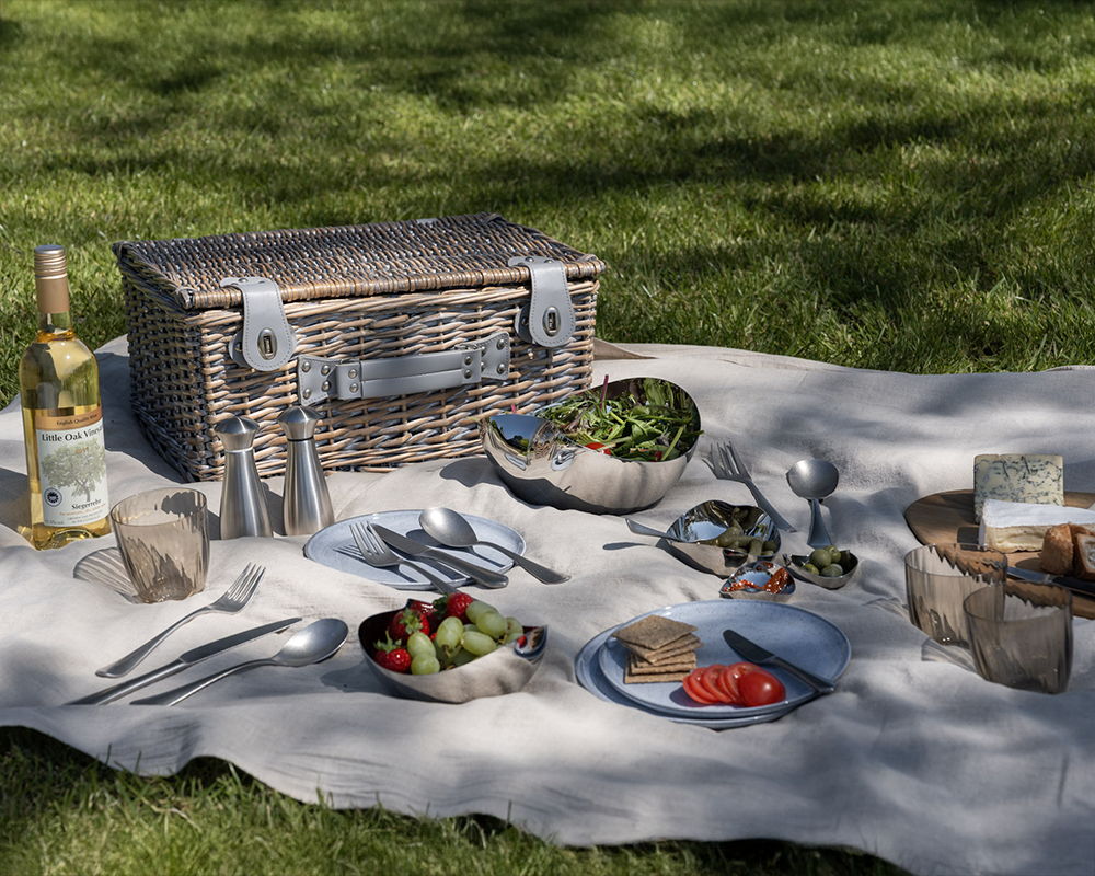 Picnic setup with a basket, food, Quinton Vintage cutlery, Signature Small Salt & Pepper Mills and serving bowls.
