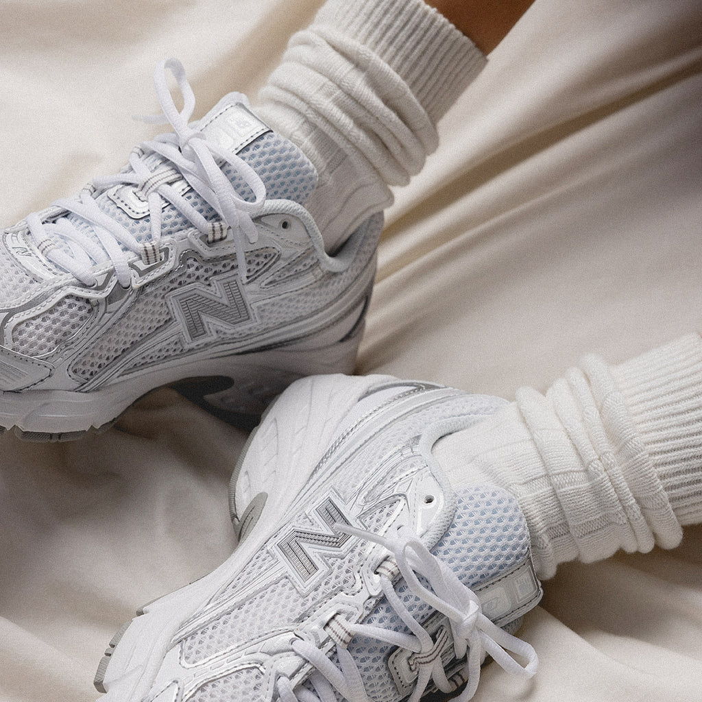 White sneakers with rolled white socks on a neutral background.