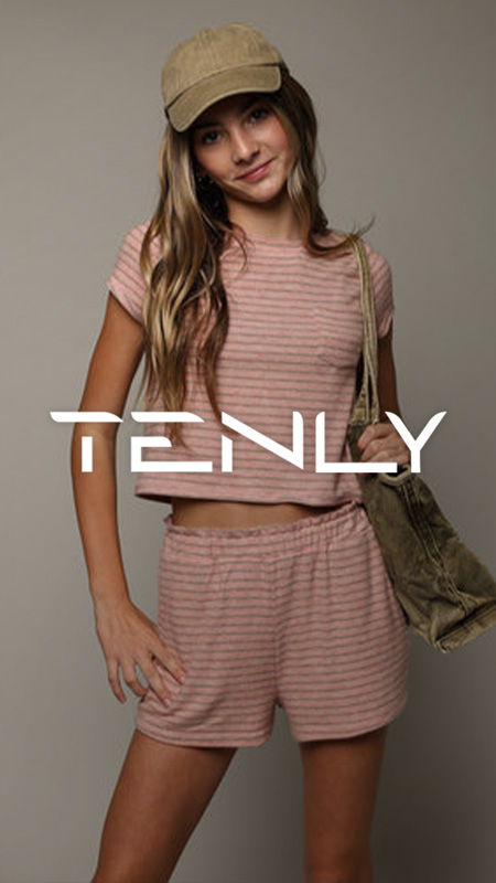 Young woman in striped outfit wearing a cap, posing with a bag.