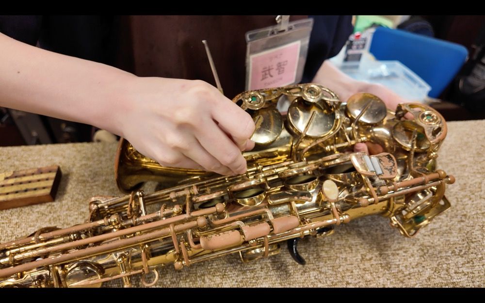 A hand cleaning or adjusting a saxophone on a workbench.