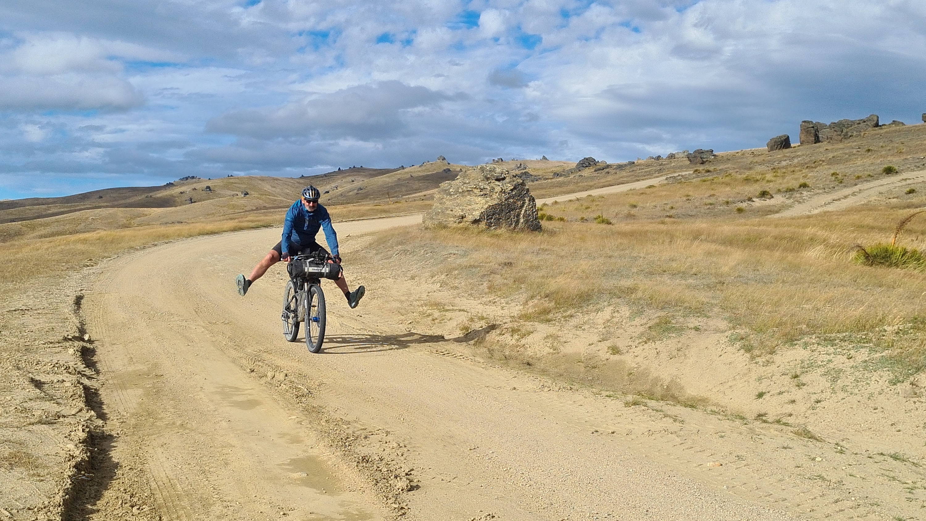 A cyclist rides down a sandy descent with both feet off the bike's pedals.