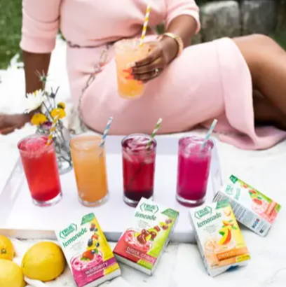 Woman in pink dress having a picnic with a variety of True Lemon drinks on her white blanket