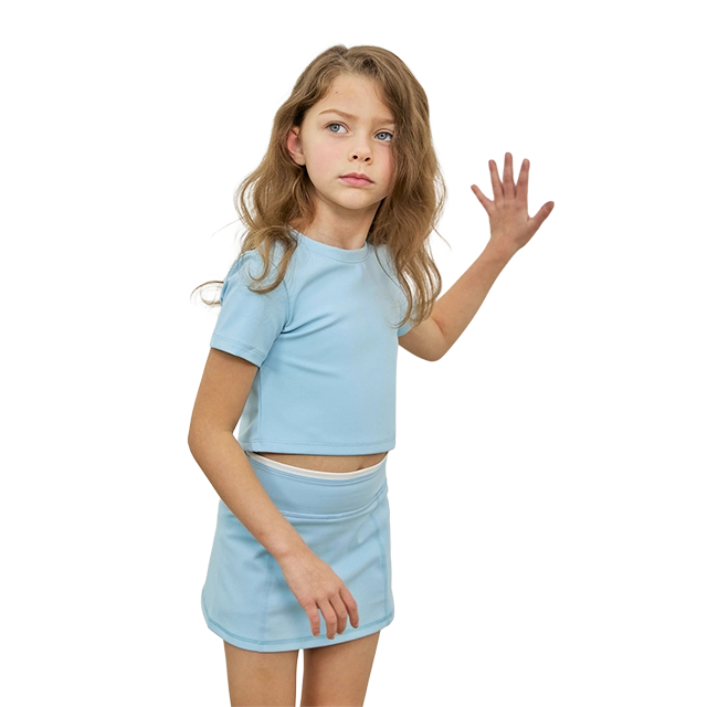 Young girl in a blue outfit, standing with her hand raised.