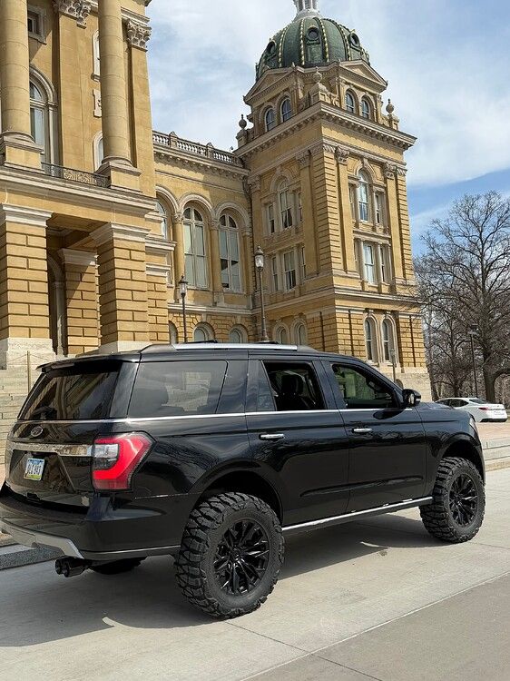 Side-rear view Troy's black 2018 Ford Expedition with off-road tires parked before yellow stone building with green dome HornBlasters Stealth Spare Tire Delete featured install gallery photo 1