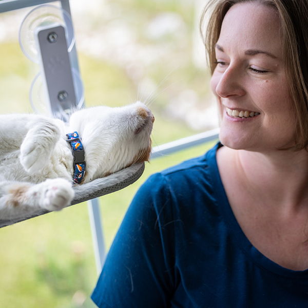 Woman smiling at a cat lounging in a window.