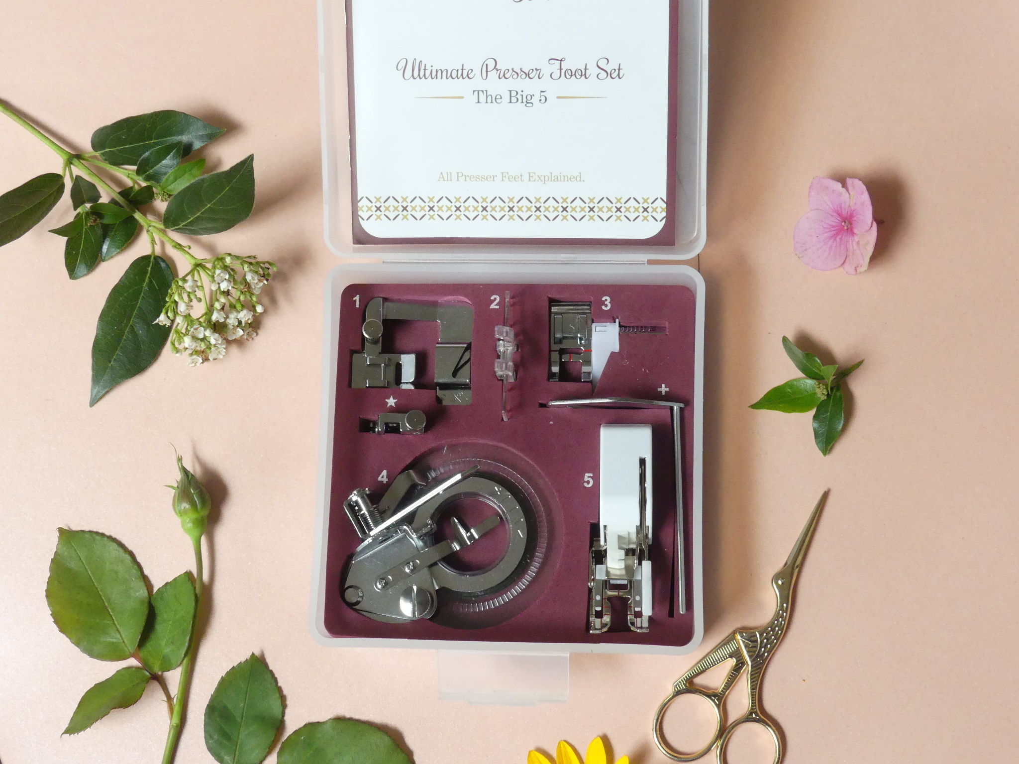the big five presser foot set on a table with flowers and stork scissors