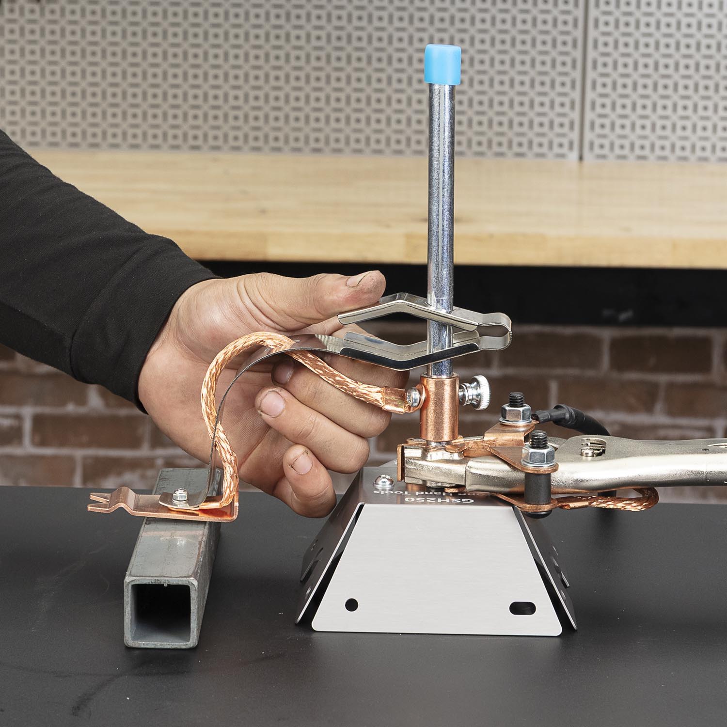 A hand holding a clamp attached to a metallic device on a table.