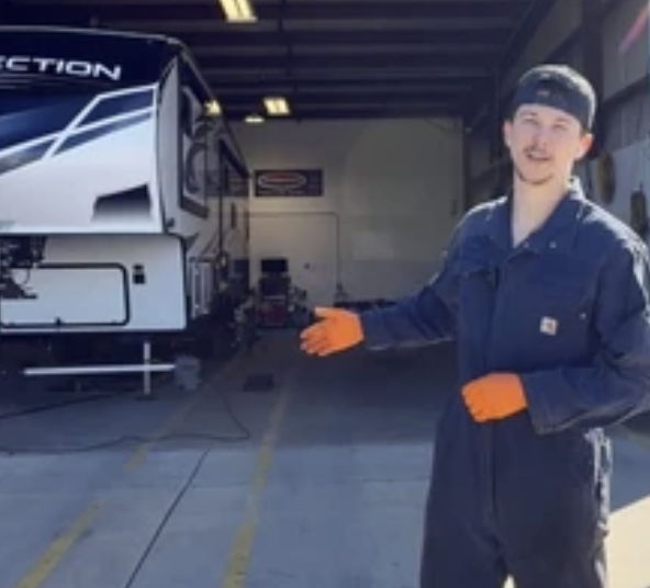 Person in work attire gesturing towards a recreational vehicle in a garage.