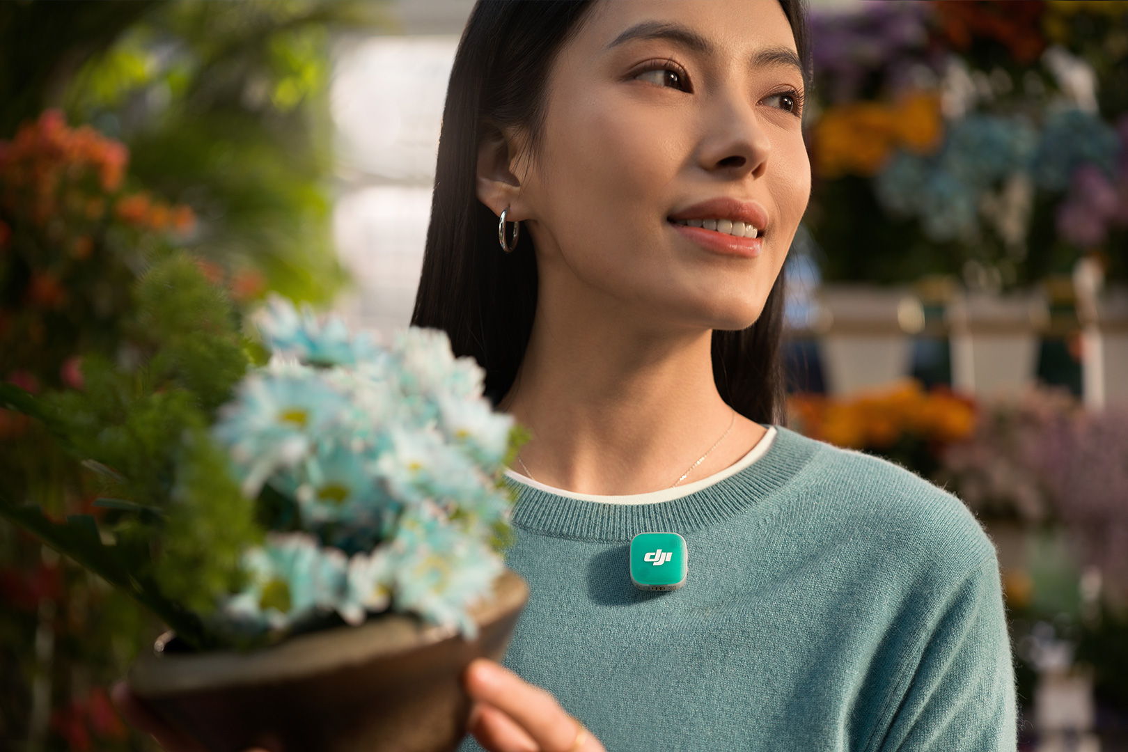 Woman holding a flower pot in a vibrant outdoor setting with a green DJI Mic Mini 2.