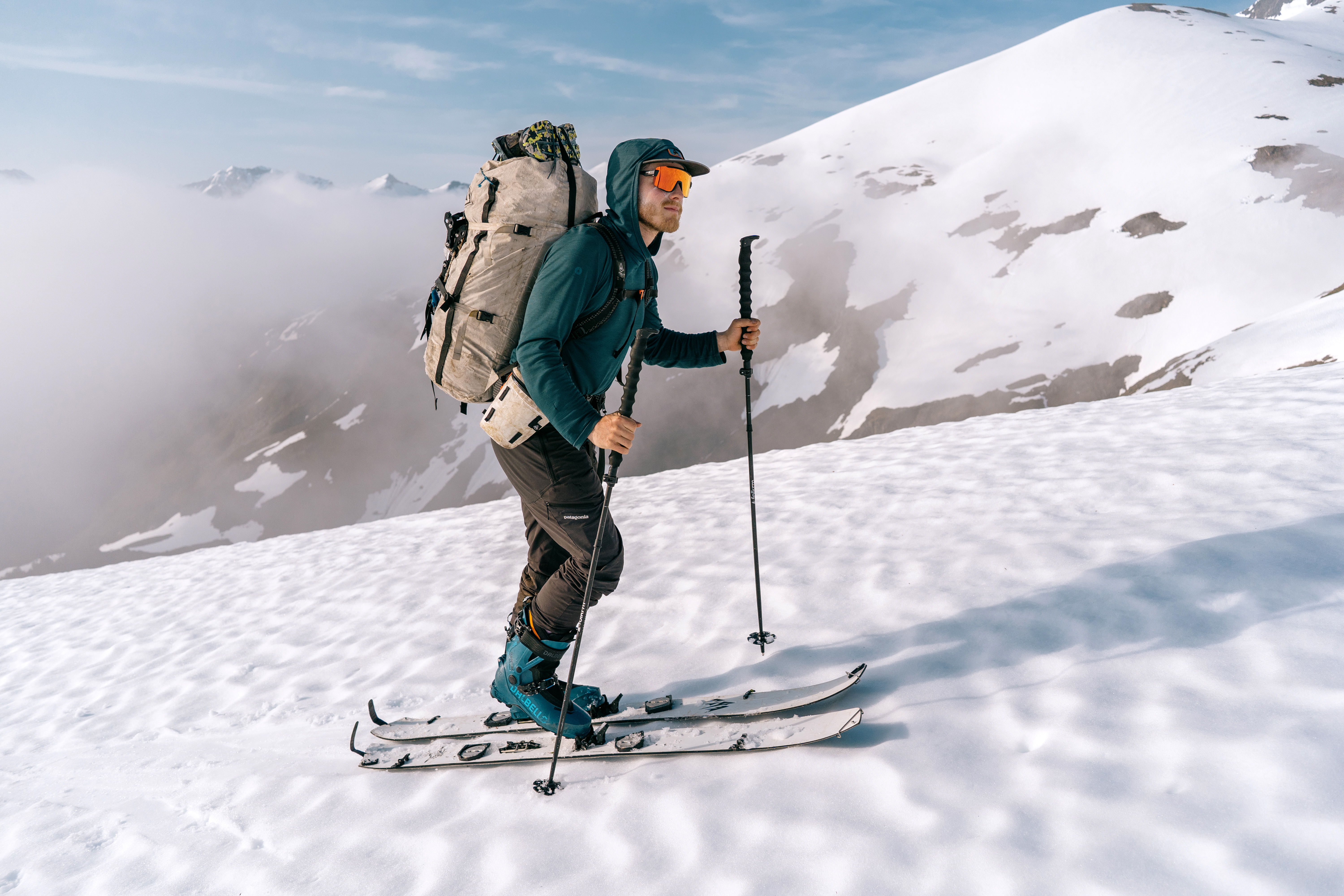Splitboarder ascending snowy mountain with backpack and snowboard poles.