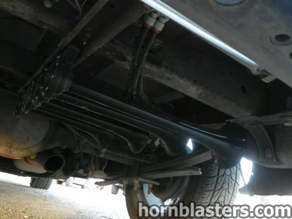 Underbody view showing long black horn components mounted along the frame of Thomas's 2005 Chevy Silverado 1500, install photo 3