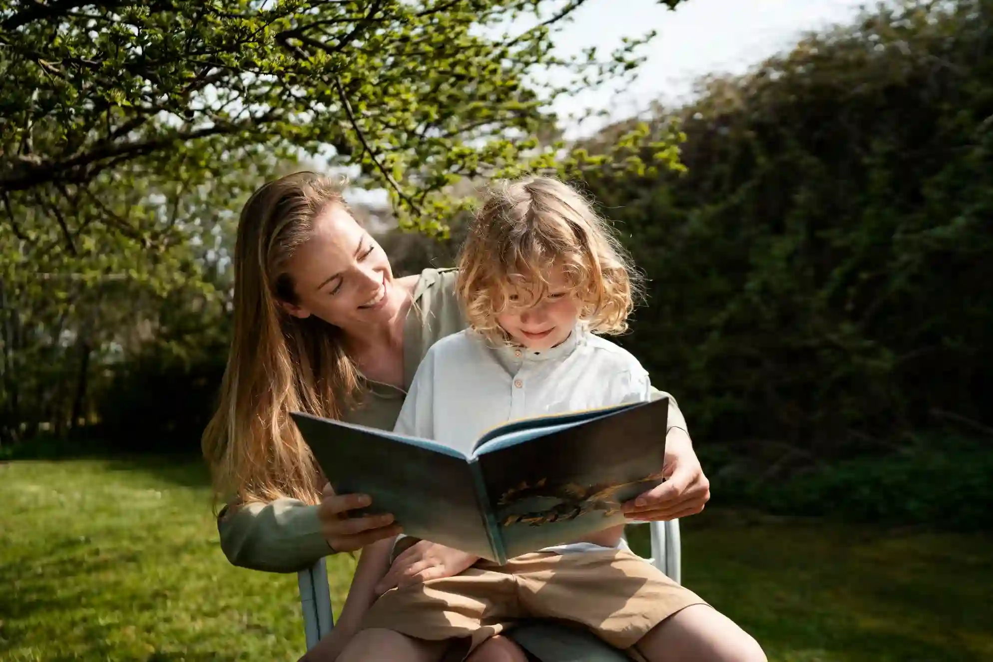 Een moeder en kind die buiten onder een boom een boek lezen.