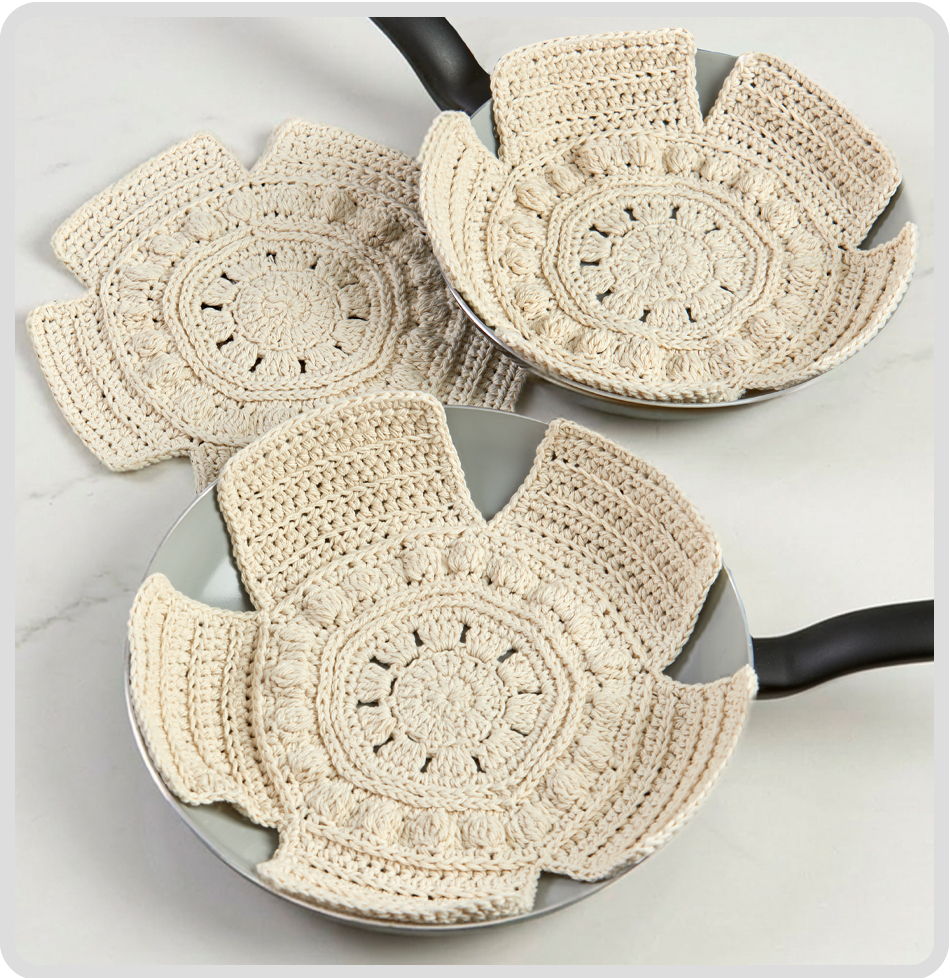 Three crocheted pot holders on frying pans.