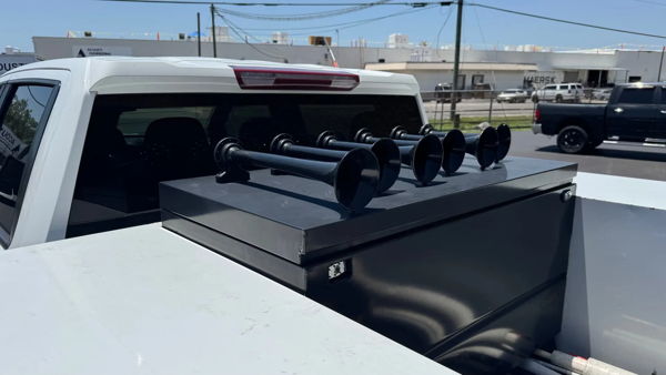 Close-up of black train horn bells mounted on a black box behind the cab of George's 2022 Chevrolet Silverado 3500 HD, install photo 5