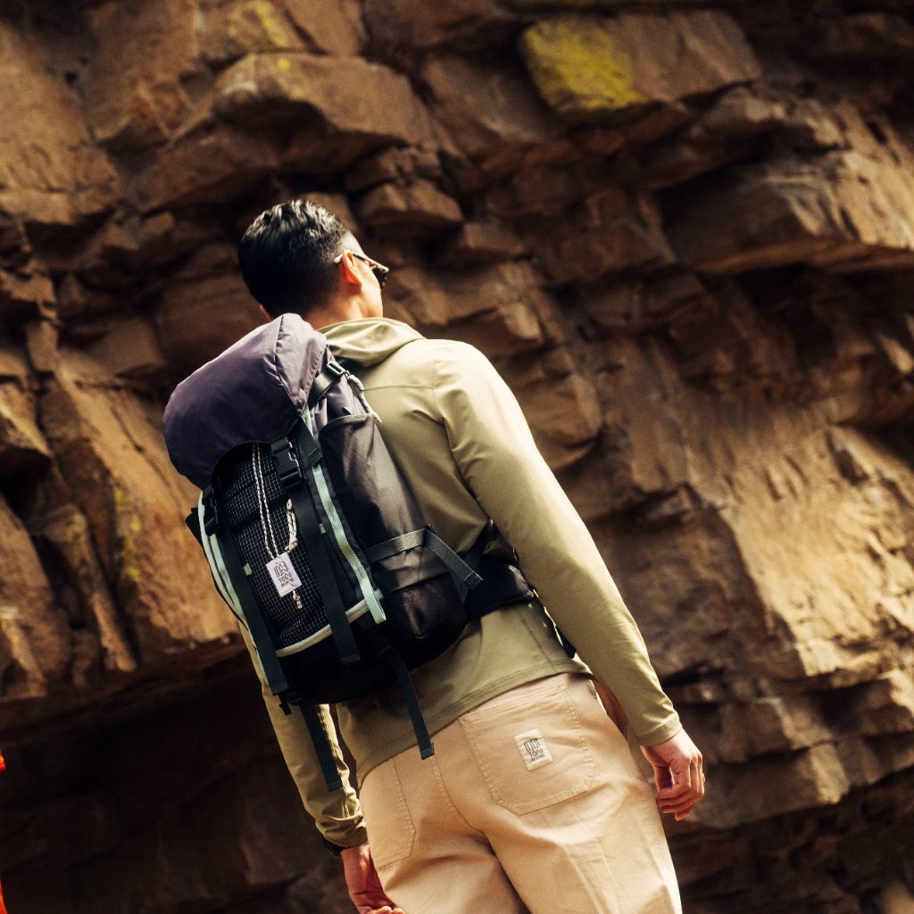 Person with a backpack standing in front of a rocky wall.