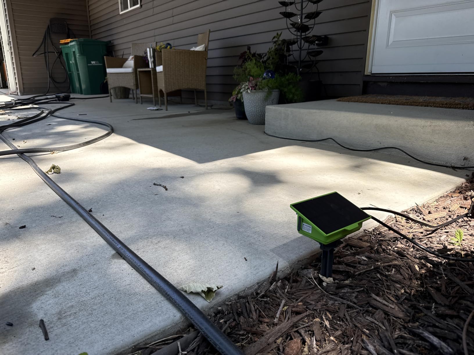 A concrete patio with a green device and garden hose nearby.