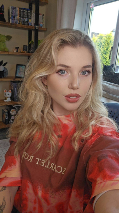 Young woman with blonde hair in a tie-dye shirt, smiling for a selfie.