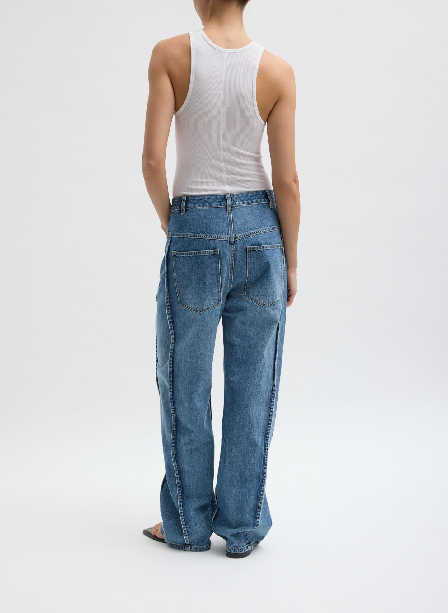 Woman wearing a tank top and blue jeans, viewed from behind.