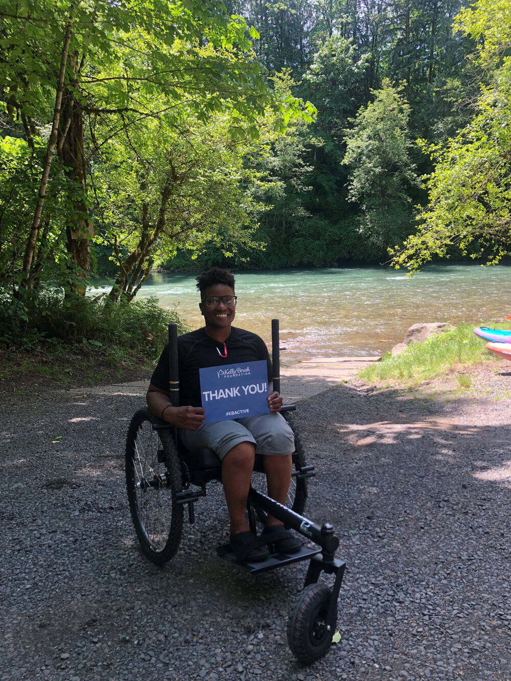 Person in GRIT Freedom Chair on gravel in front of water and trees holding 