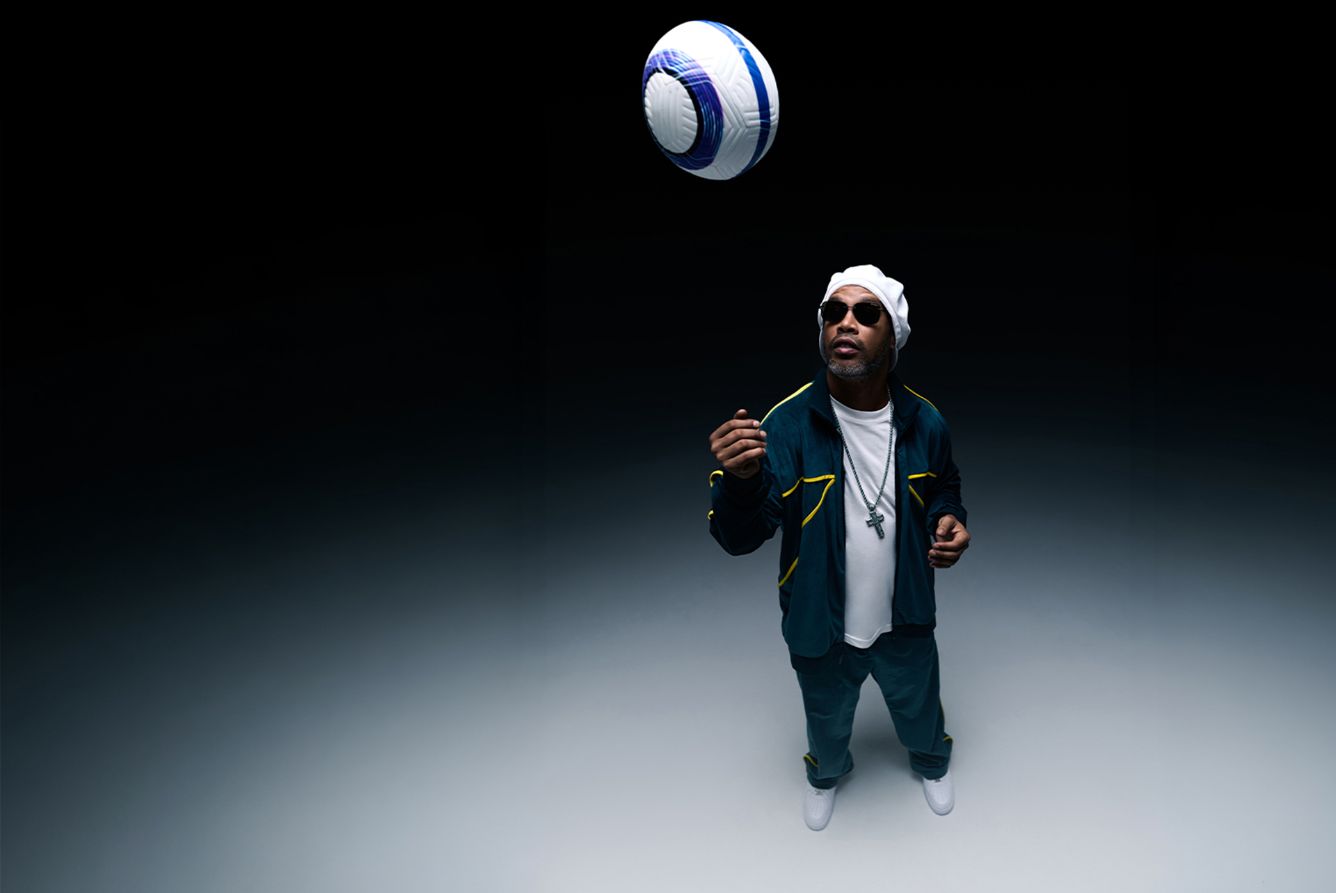 Ronaldinho in sportswear juggling a soccer ball against a dark background.