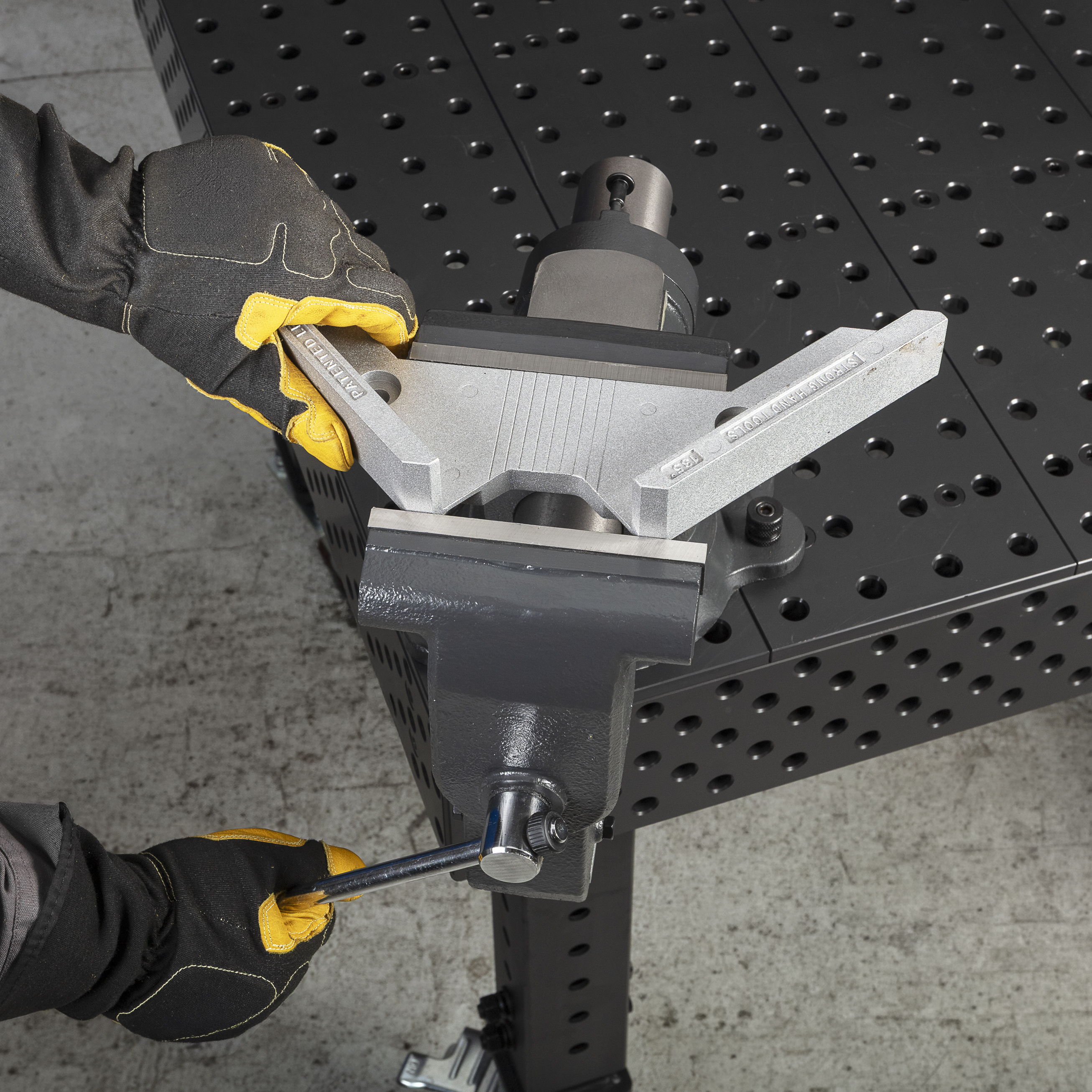 Hands adjusting a vice grip on a workbench with a textured surface.