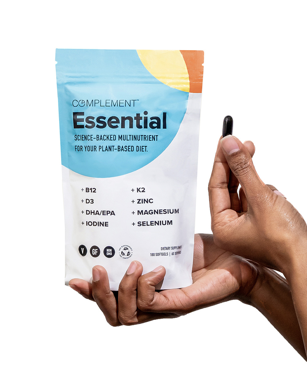 Hand holding Complement Essential vegan multivitamin capsules and pouch. 