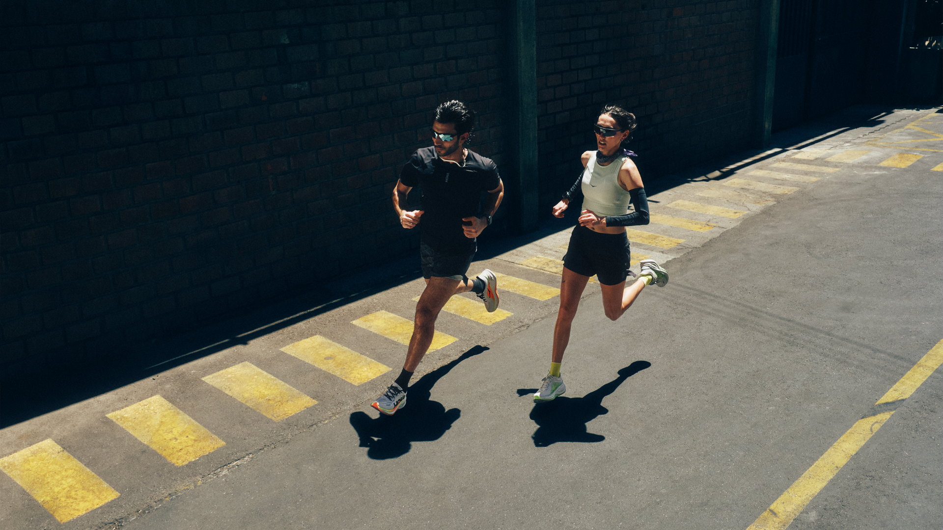 Two runners jogging on a sunny street with yellow crosswalk lines.