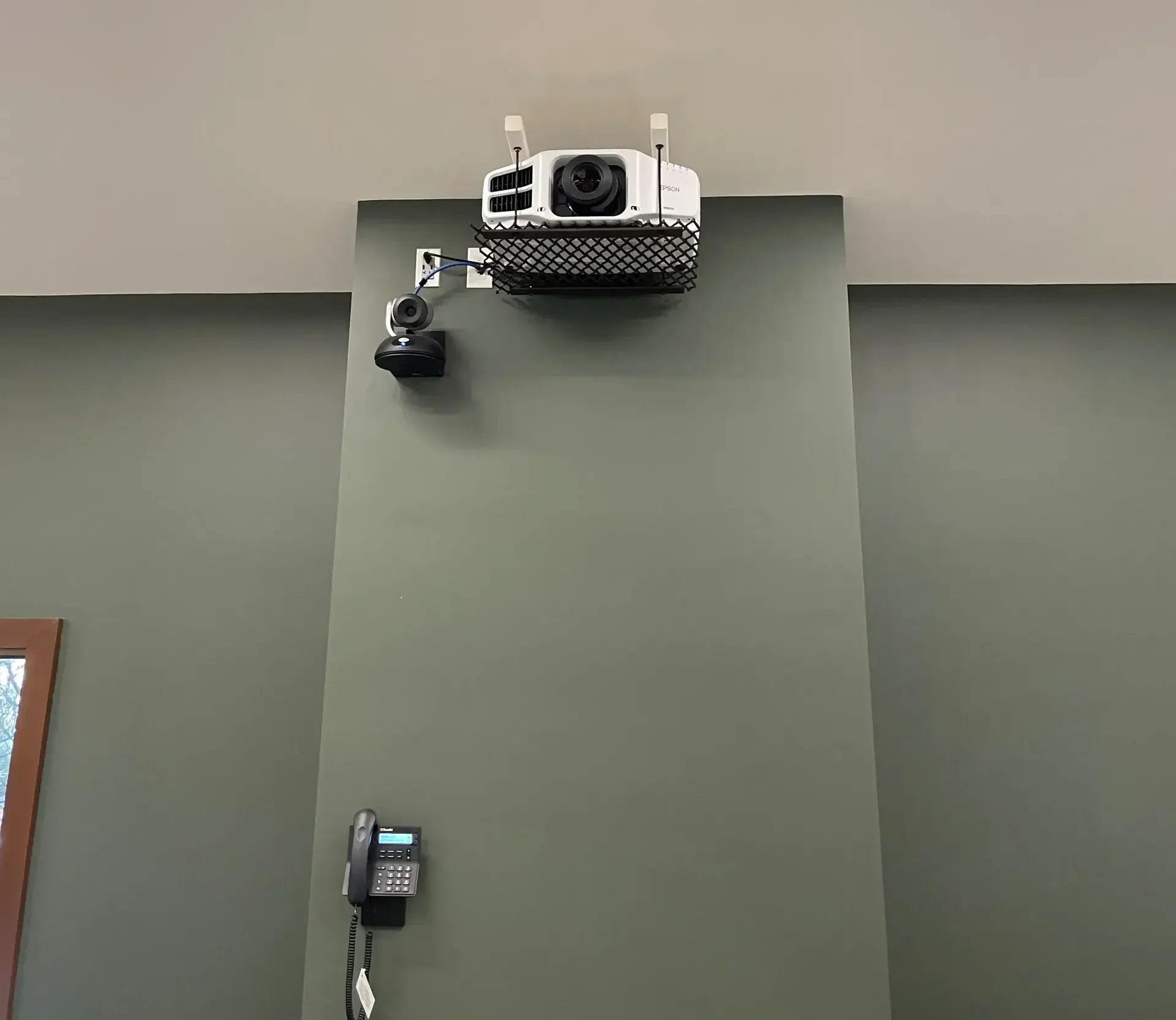 Projector mounted on a green wall with a camera and control panel.