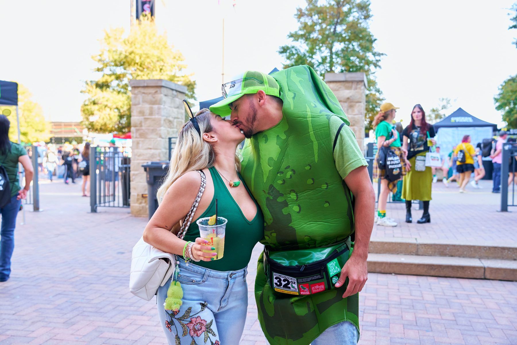 Couple kissing with one in a pickle costume and Grillo's Pickles fanny pack at The Big Dill Arlington Texas 2025.