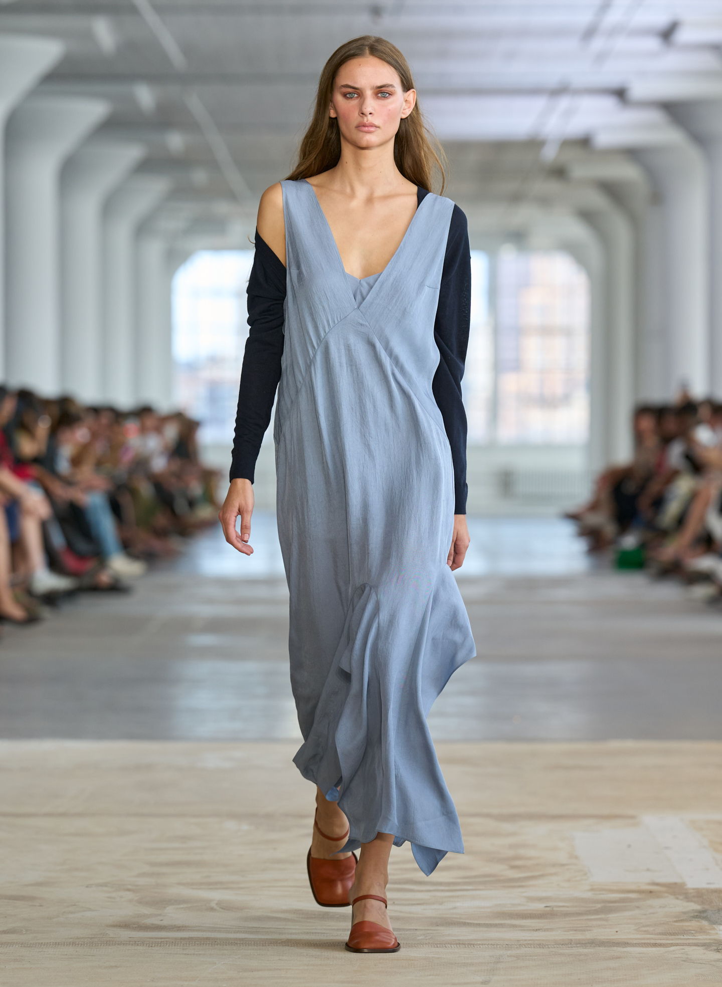 Model walking down runway in a flowing blue dress and brown sandals.