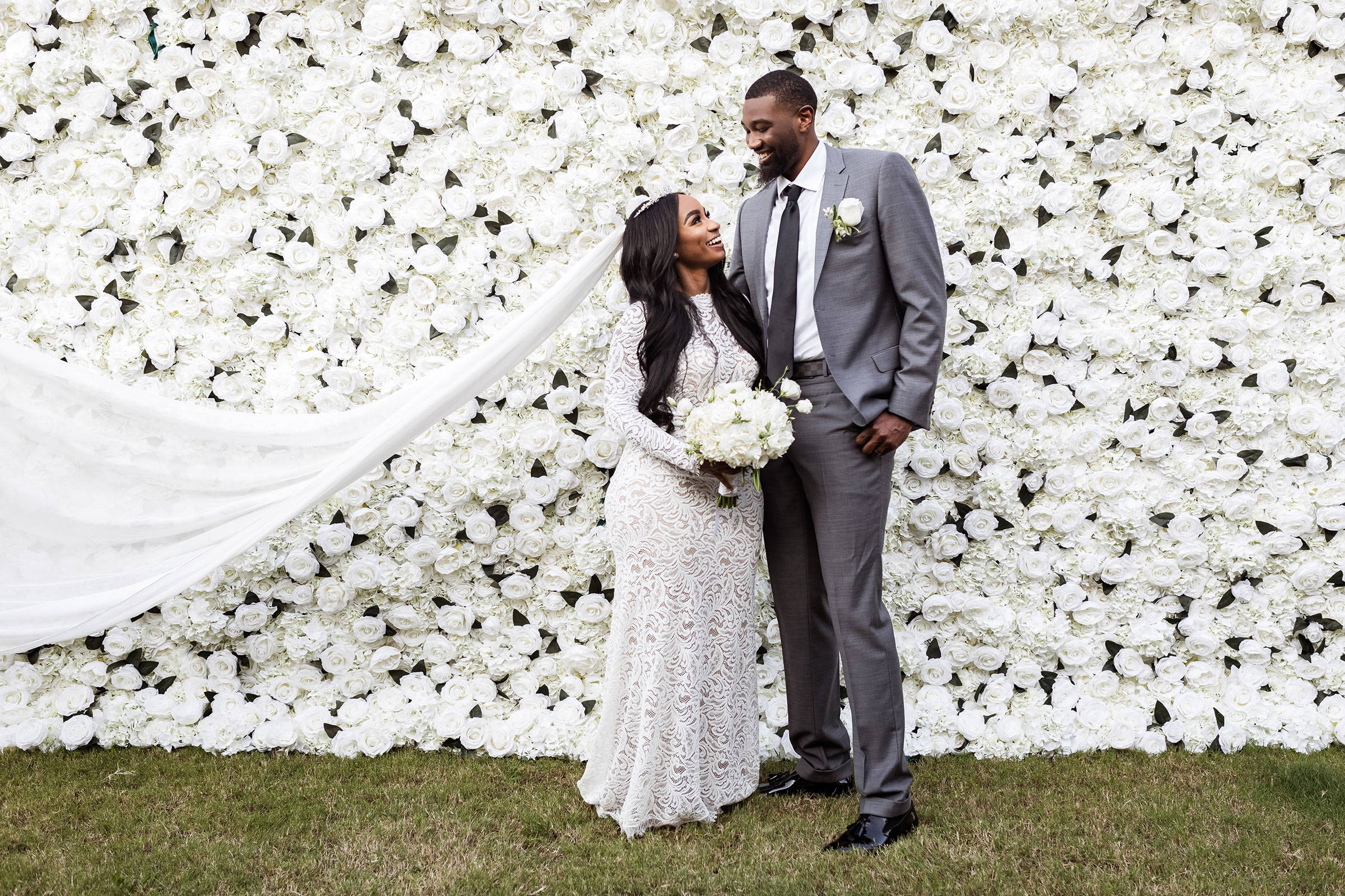 Bride wearing a long veil and lace dress and groom is in a grey suit