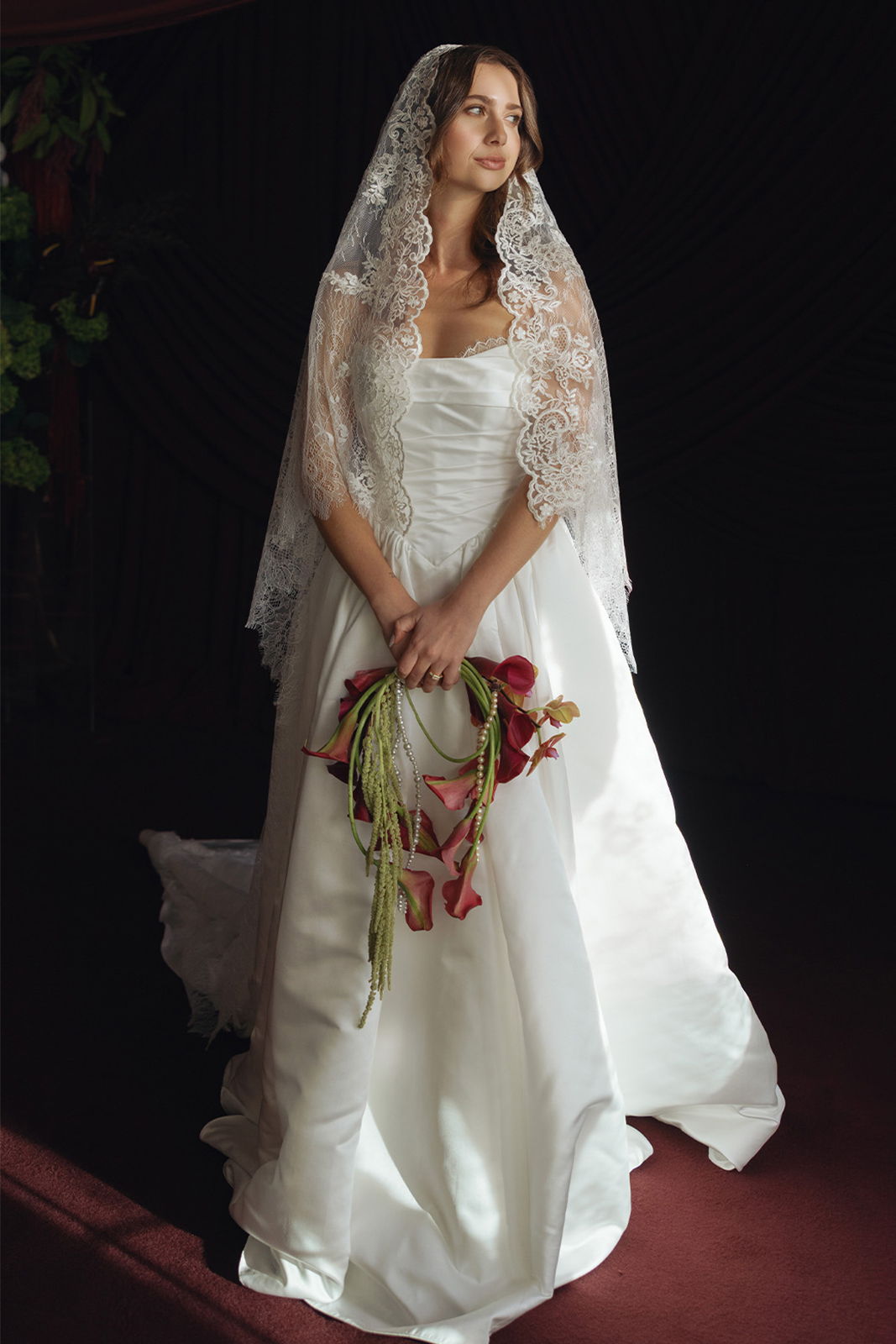 Bride in a white gown holding a bouquet, standing against a dark background.