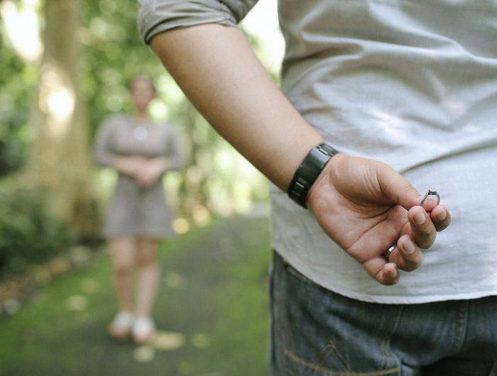 Man holding engagement ring behind back