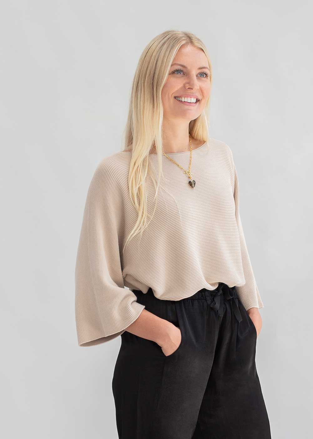 A model wearing a slouchy beige knitted sweater and black trousers