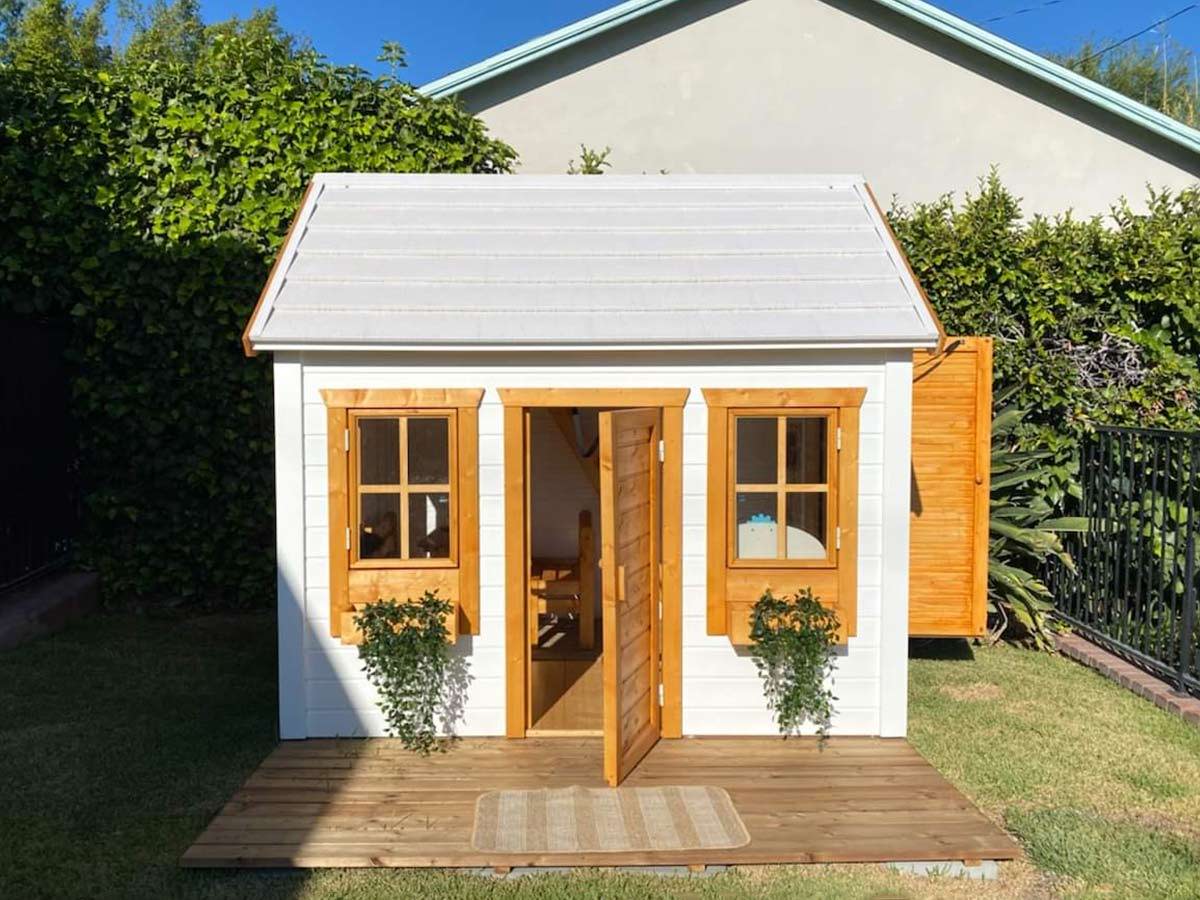 White Outdoor Playhouse with light brown Flower boxes, window trims and two doors in a backyard by WholeWoodPlayhouses