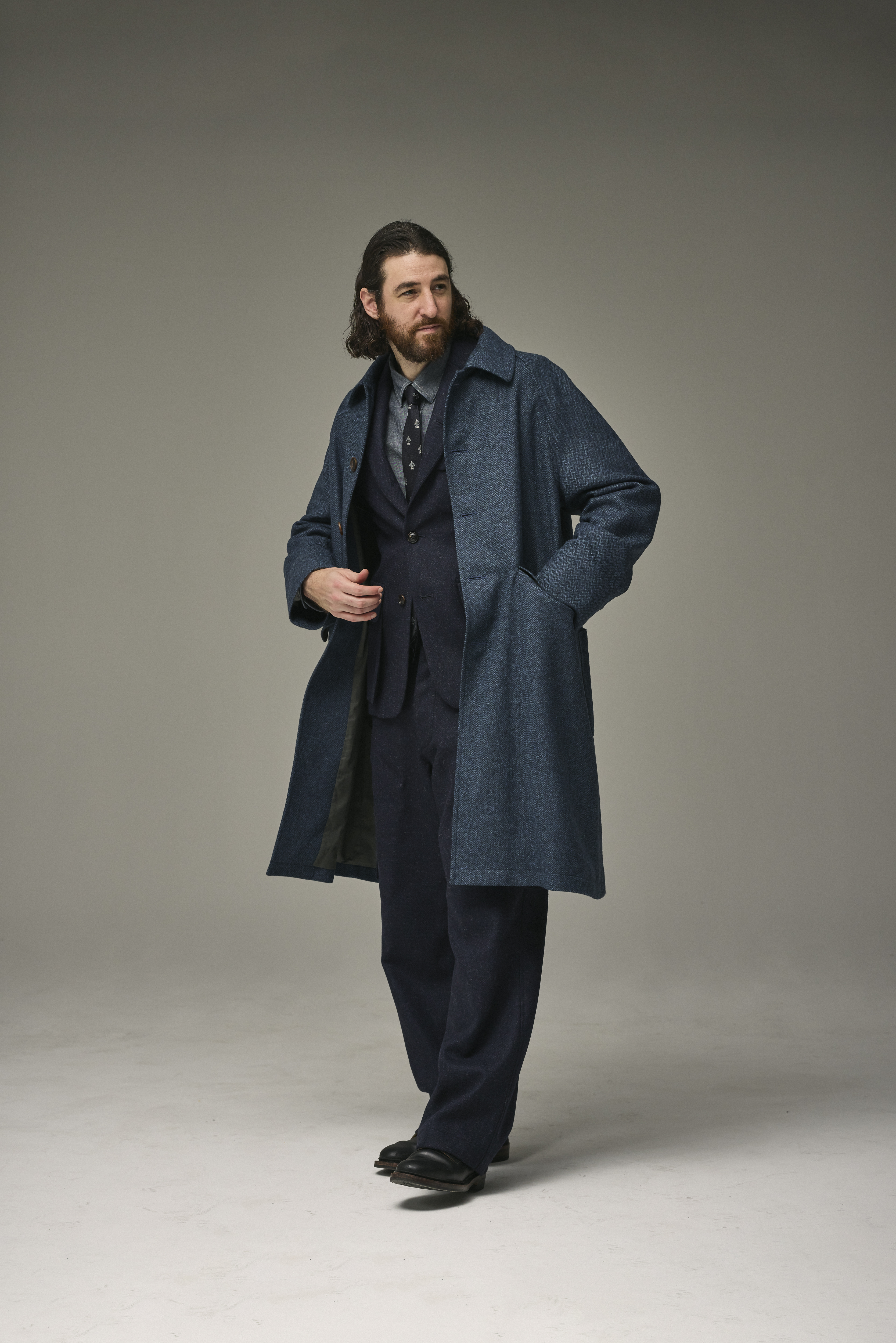 Man in a dark coat and suit, posing against a neutral background.