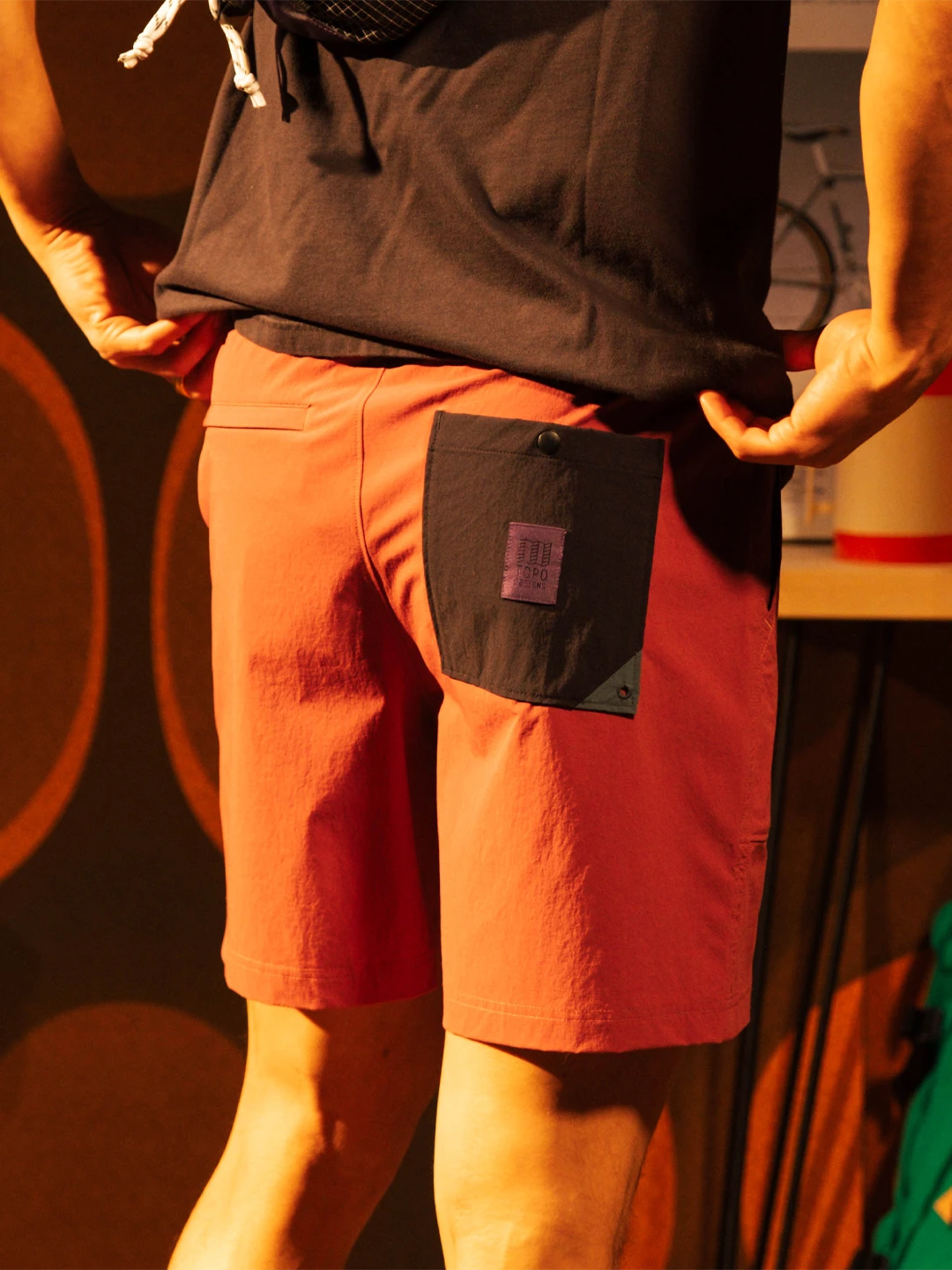Person wearing red shorts with a black pocket, standing indoors.