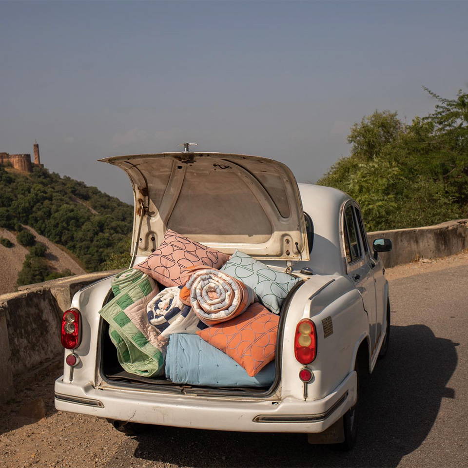 The open boot of a car on the road in Jaipur filled with colourful cushions and quilts.
