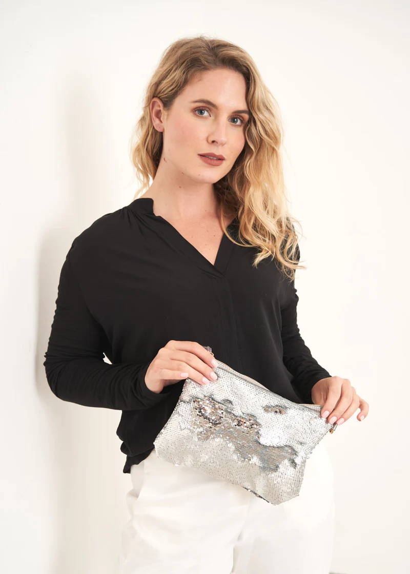 A model wearing a black long sleeve top and holding a silver sequin clutch bag
