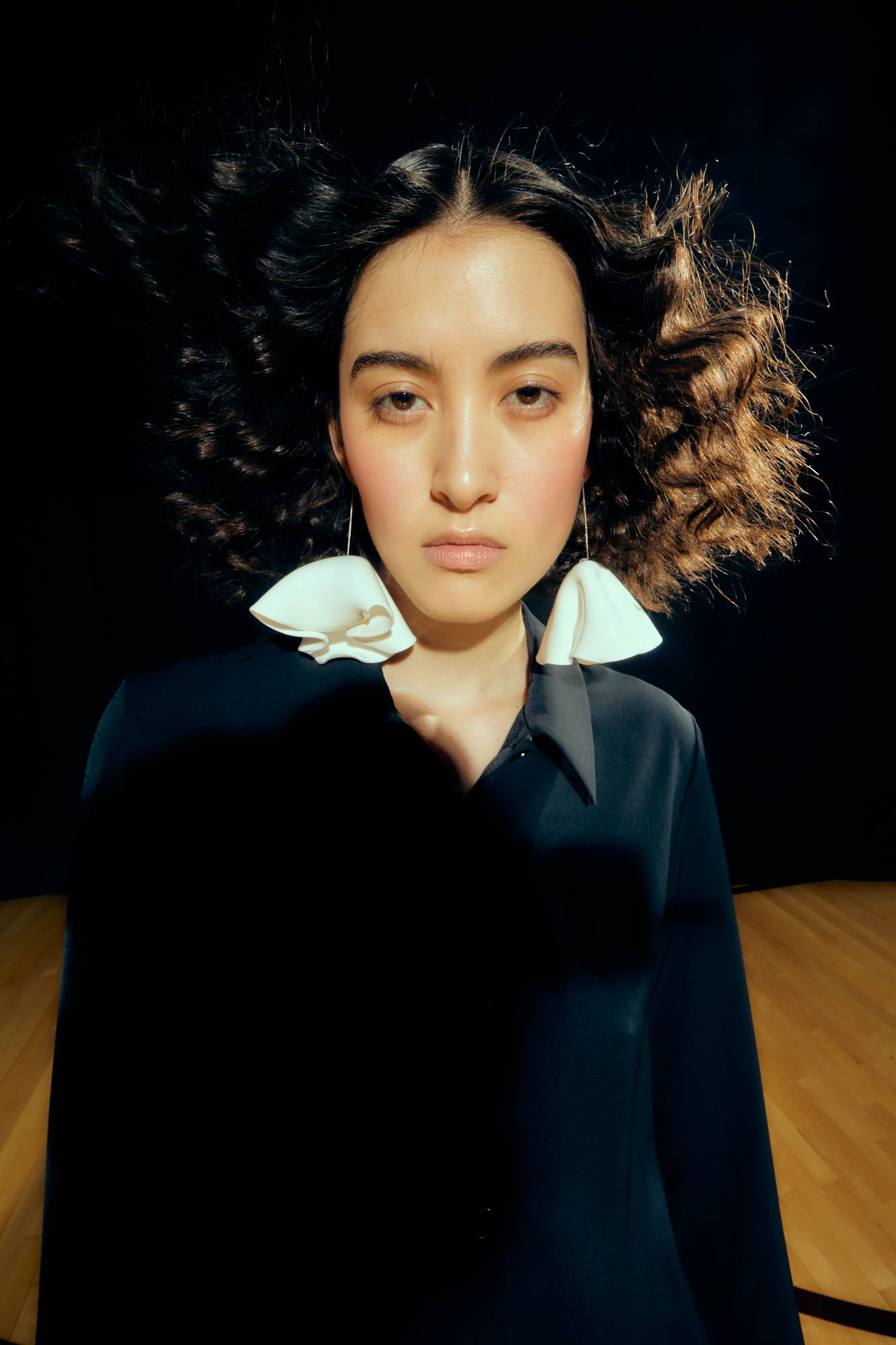 A woman with curly hair and a large collar in a dark setting.