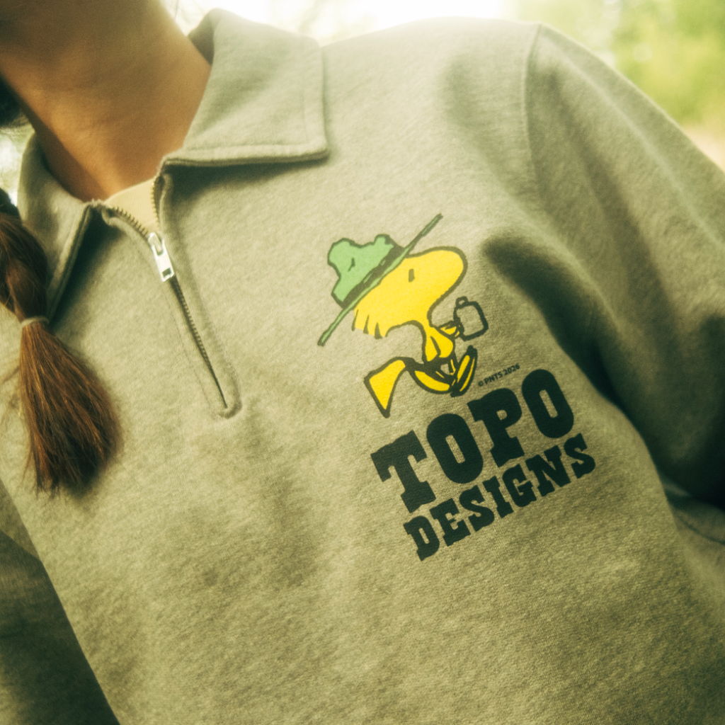Person wearing a gray sweatshirt with Topo Designs logo and cartoon character.