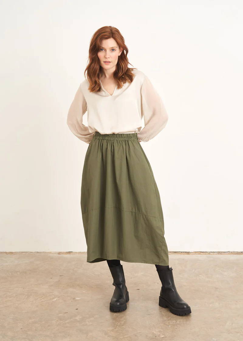 A model wearing a tulip shaped khaki green skirt with an off white top and black chunky boots