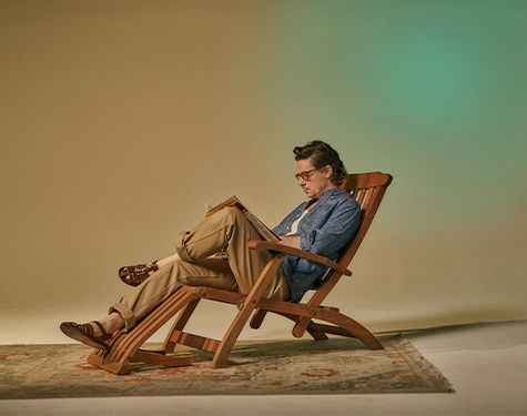 Person sitting in a wooden chair, reading, with a neutral background.