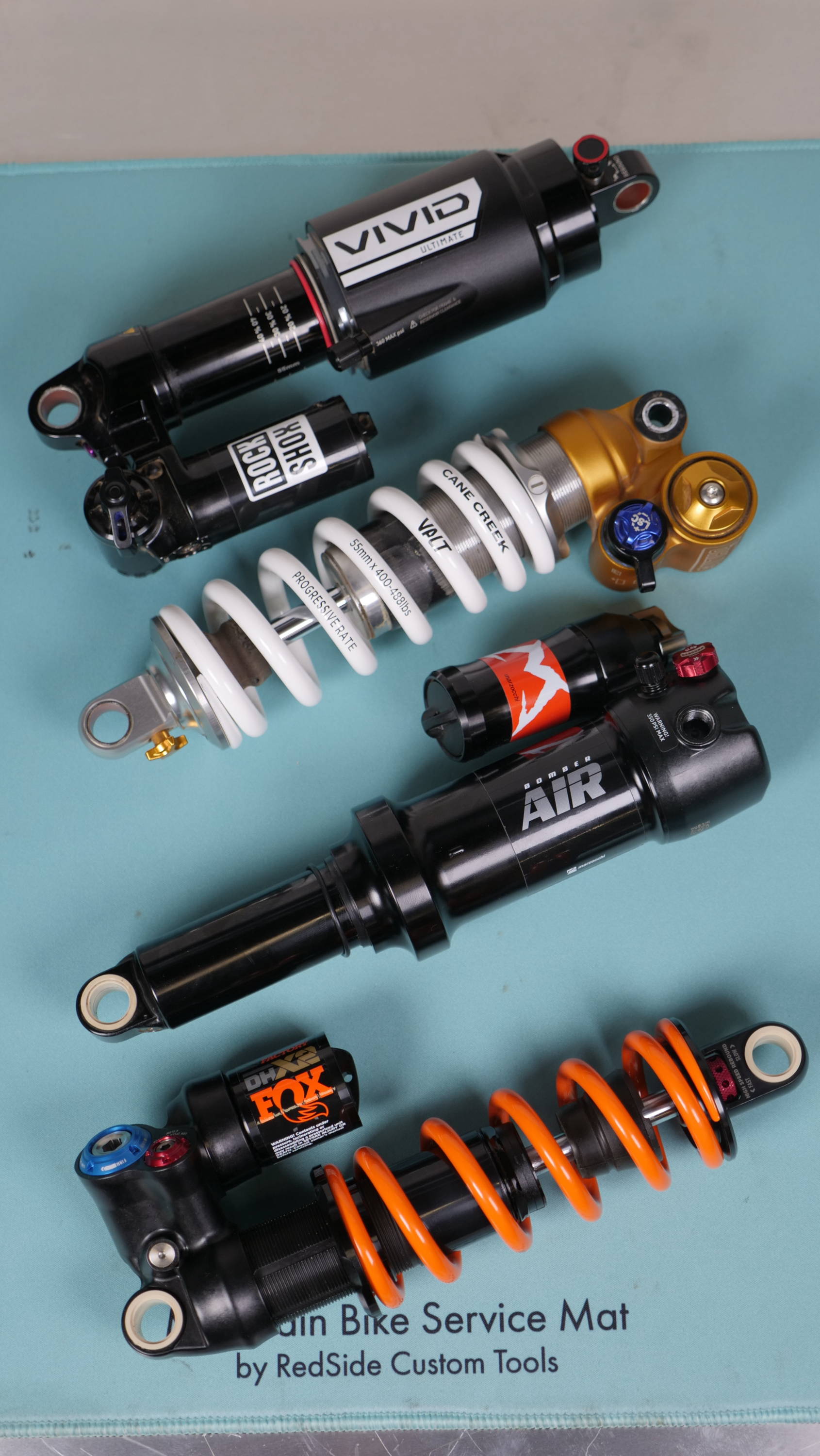 RockShox Vivid, Ohlins ttx22, Marzocchi Bomber Air, and Fox DHX2 sitting next to each other on a mat