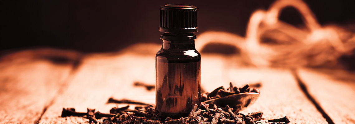 Brown glass bottle surrounded by cloves on a wooden surface.