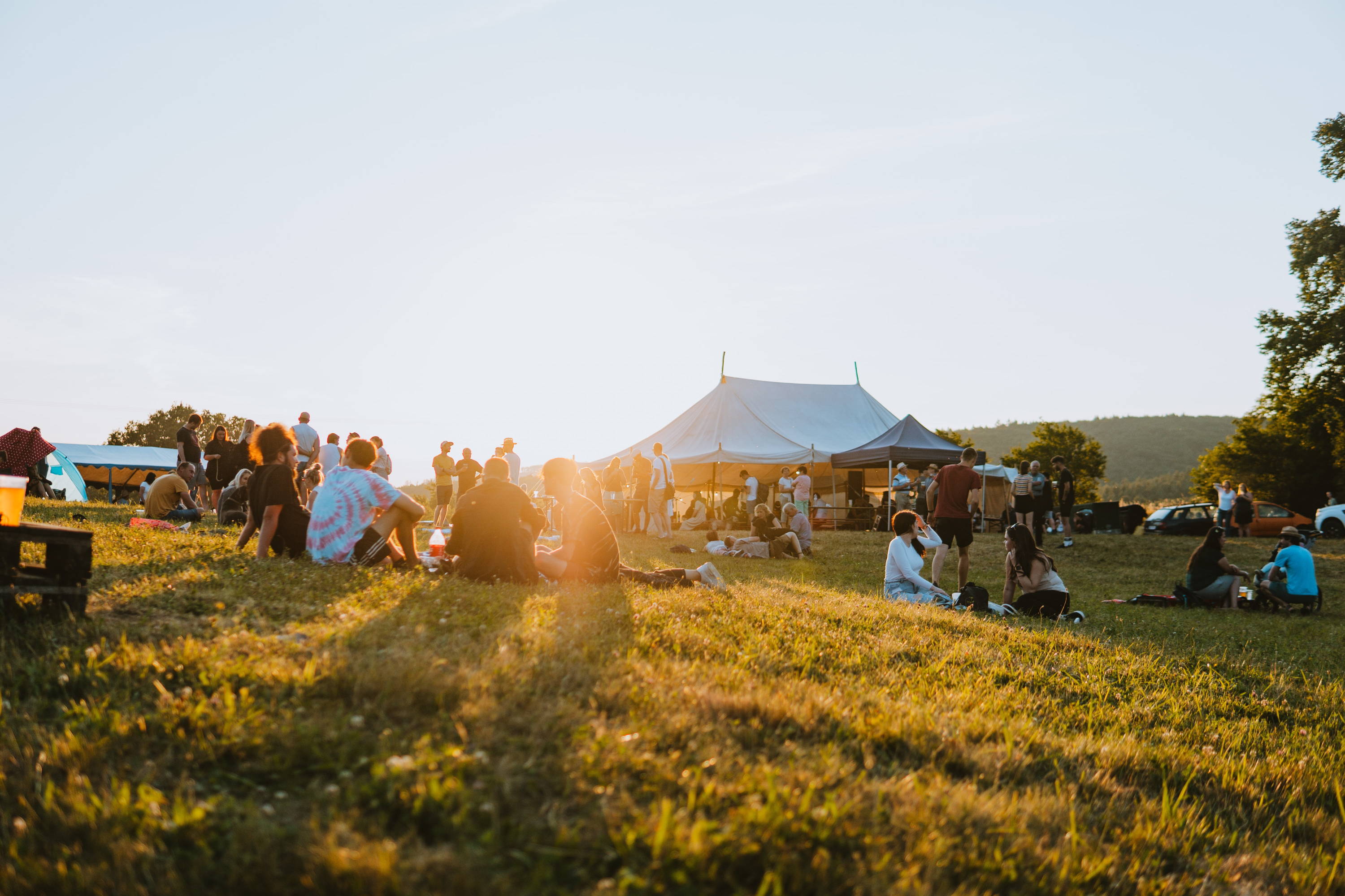 A field at sunset with festival tents and people sitting on the grass