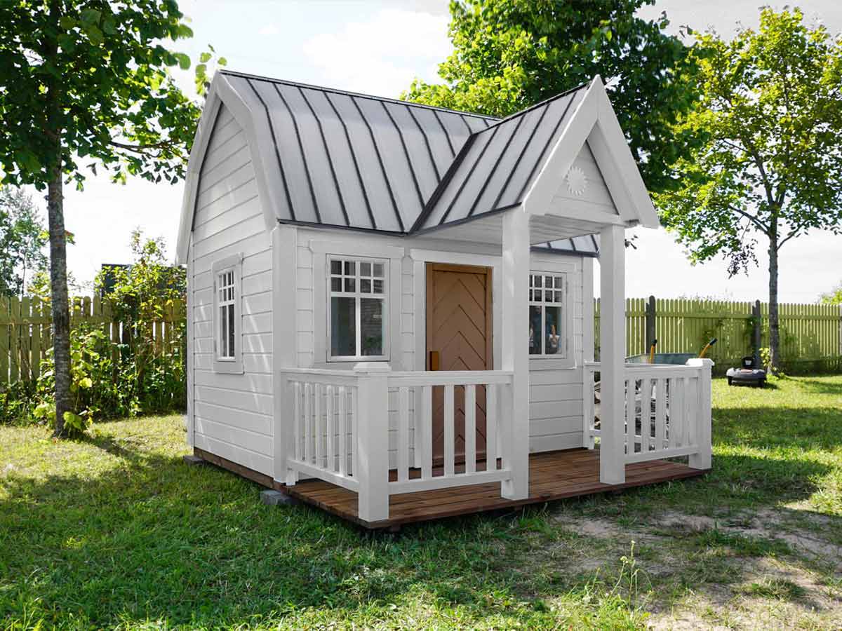 Custom playhouse in farmhouse style with white walls and terrace in a green garden by WholeWoodPlayhouses