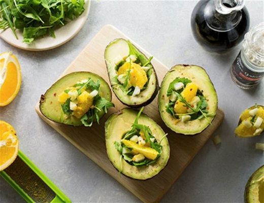 Avocado halves topped with greens and citrus on a cutting board.