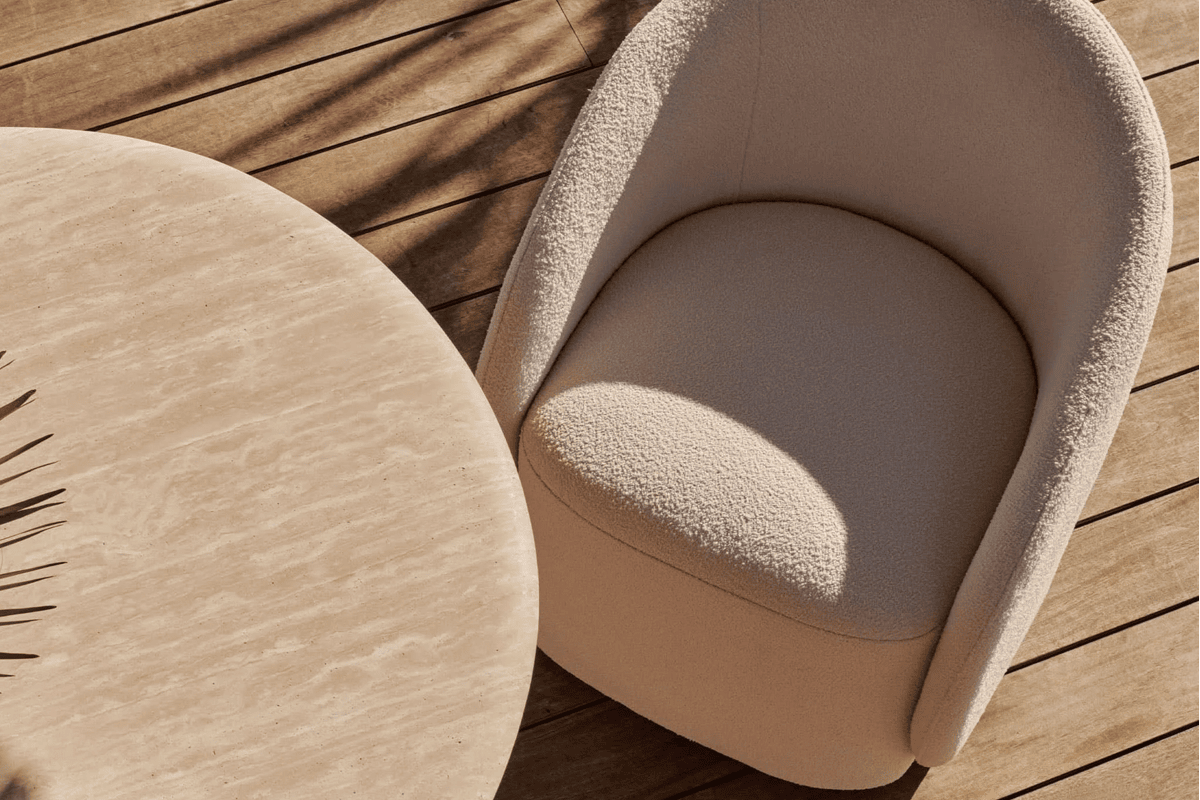 Close-up of a boucle-style outdoor dining chair beside a round travertine-look table on a wood deck in warm sunlight.